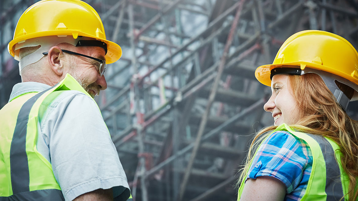 PM March 2024 Kenny Chapman column feature image of mature male and young female building workers smile together